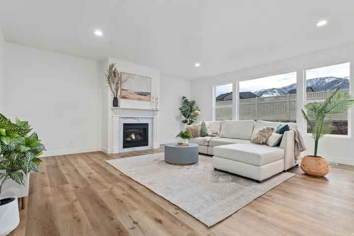 Recessed lighting, wood-finish flooring, white walls, large windows, and a fireplace with a marble-finish surround