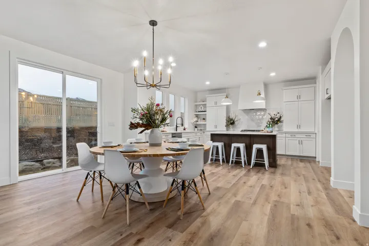 Open-concept living area with wood-finish flooring, a contemporary chandelier, white cabinetry, a kitchen island with seating, and a large sliding glass door