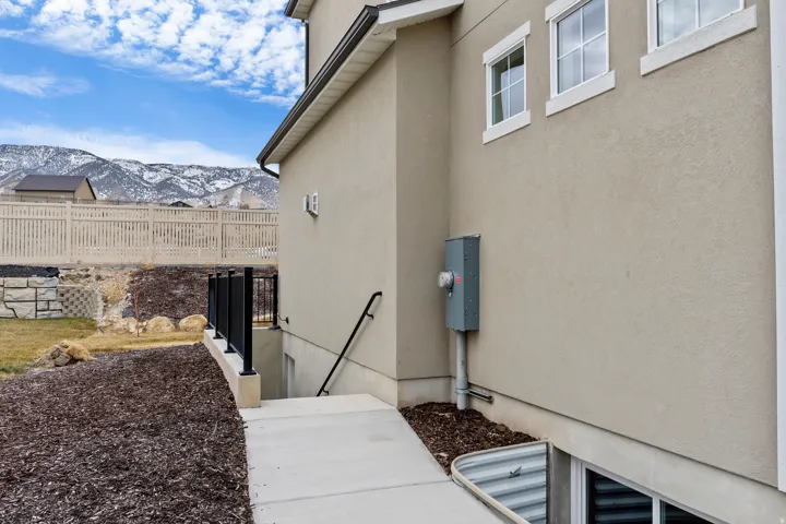 Stucco exterior with white-framed windows, concrete pathway to a lower level, black metal railings, and a fenced yard