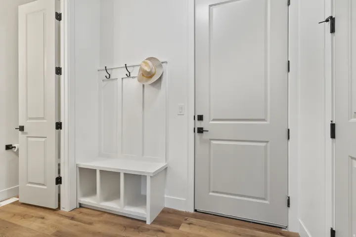 Built-in white storage bench with open cubbies, wall-mounted coat hooks, and durable wood-finish flooring