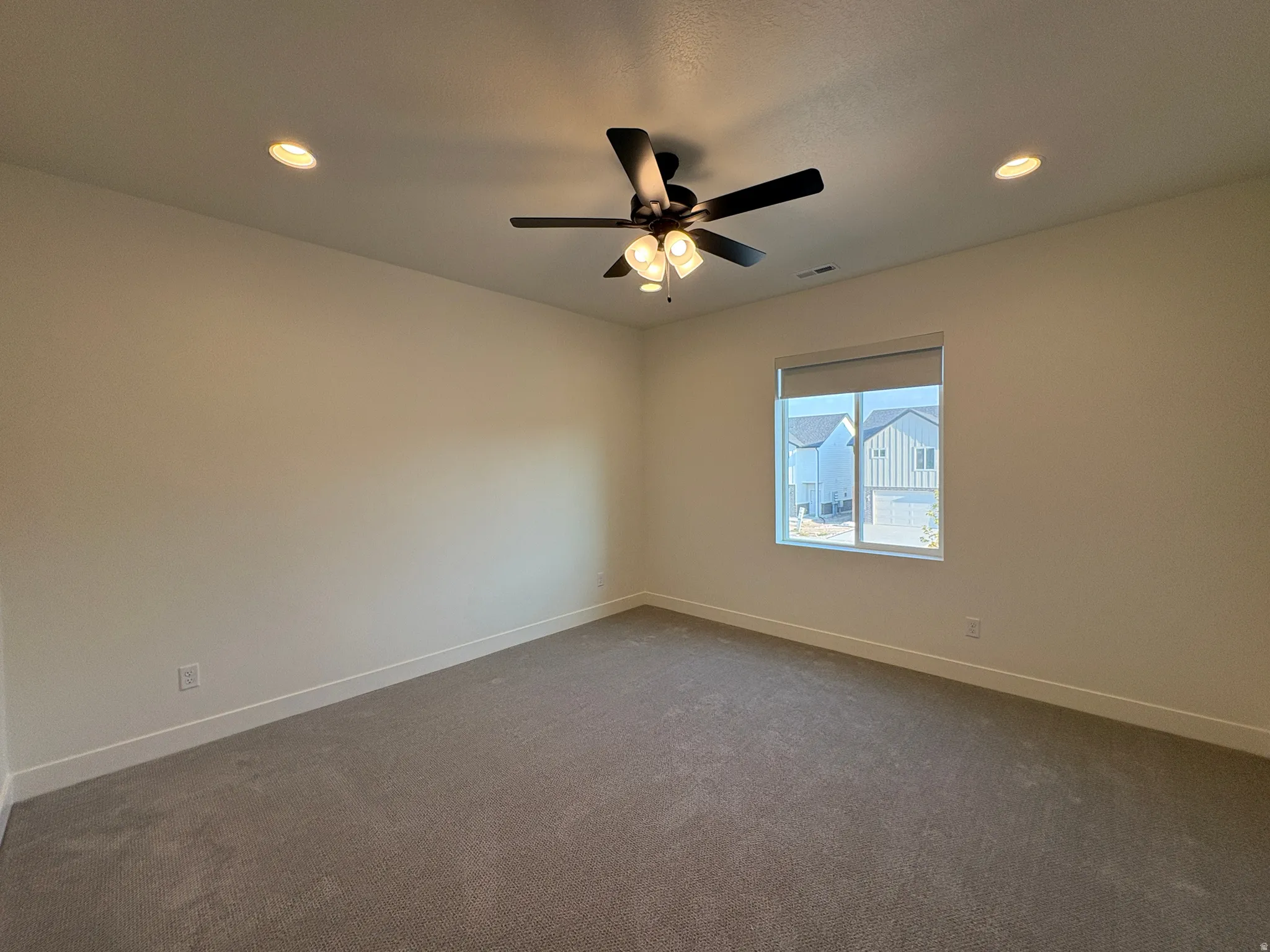 Recessed lighting, ceiling fan, window with roller shade, and neutral-toned carpeting