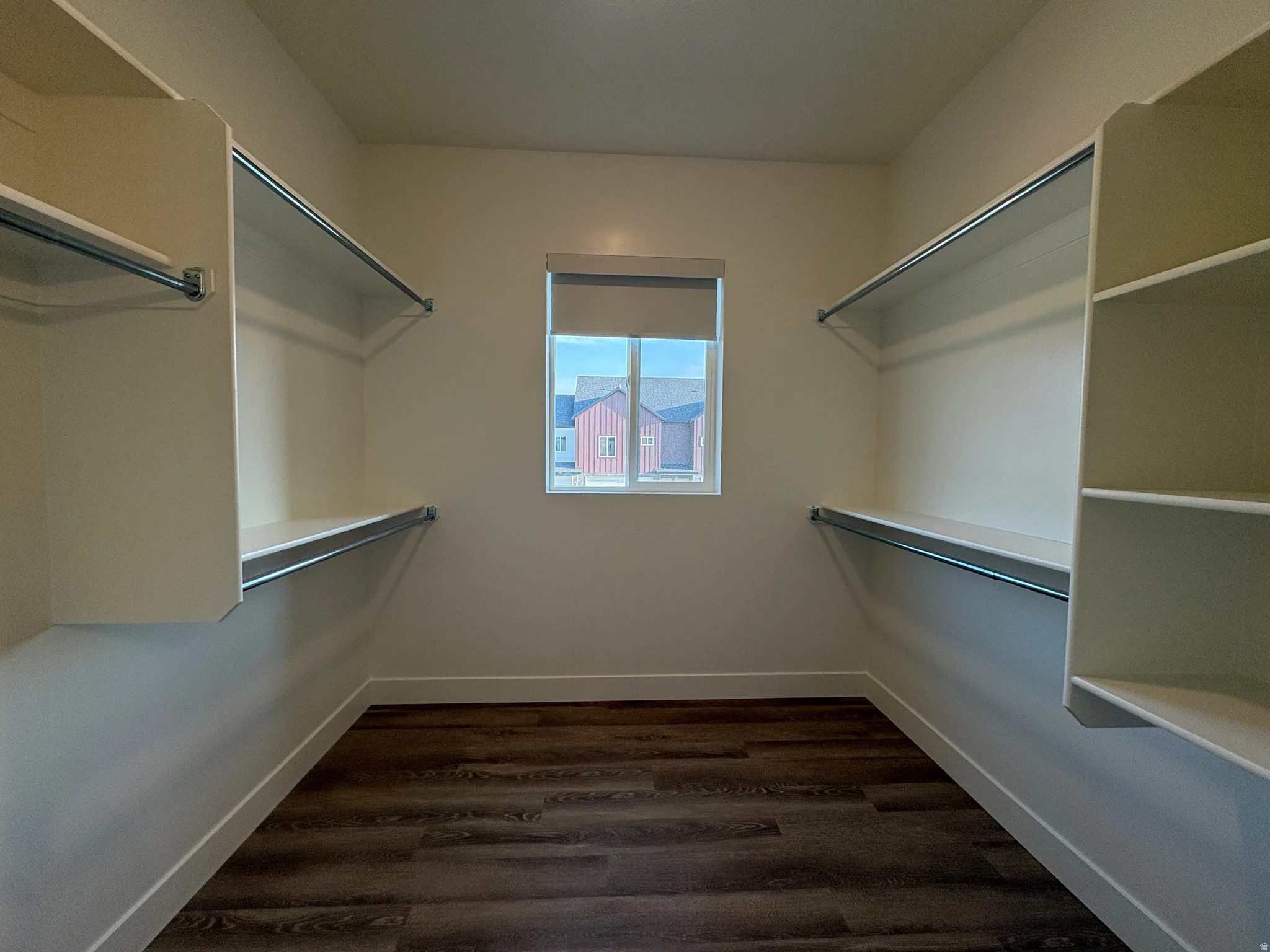 Walk-in closet featuring wood-finish flooring, built-in shelving, hanging rods, and a window with a roller shade