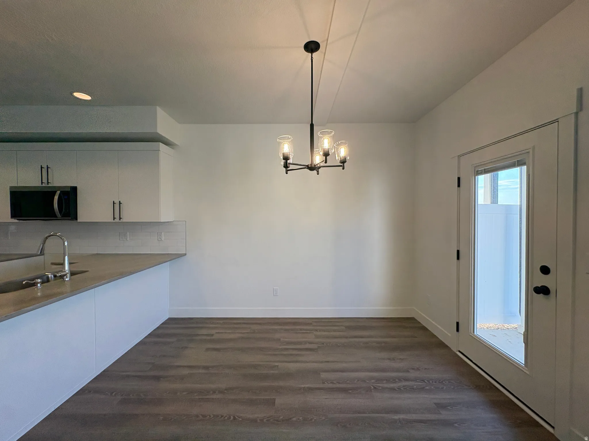 Open-concept living area with wood-finish flooring, a modern chandelier, and a glass-paneled door