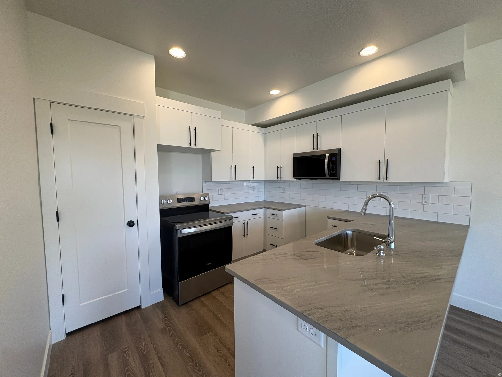(Stove still needs to be set) Modern kitchen featuring white cabinetry, a subway tile backsplash, stainless steel appliances, wood-finish flooring, and a kitchen island with an undermount sink