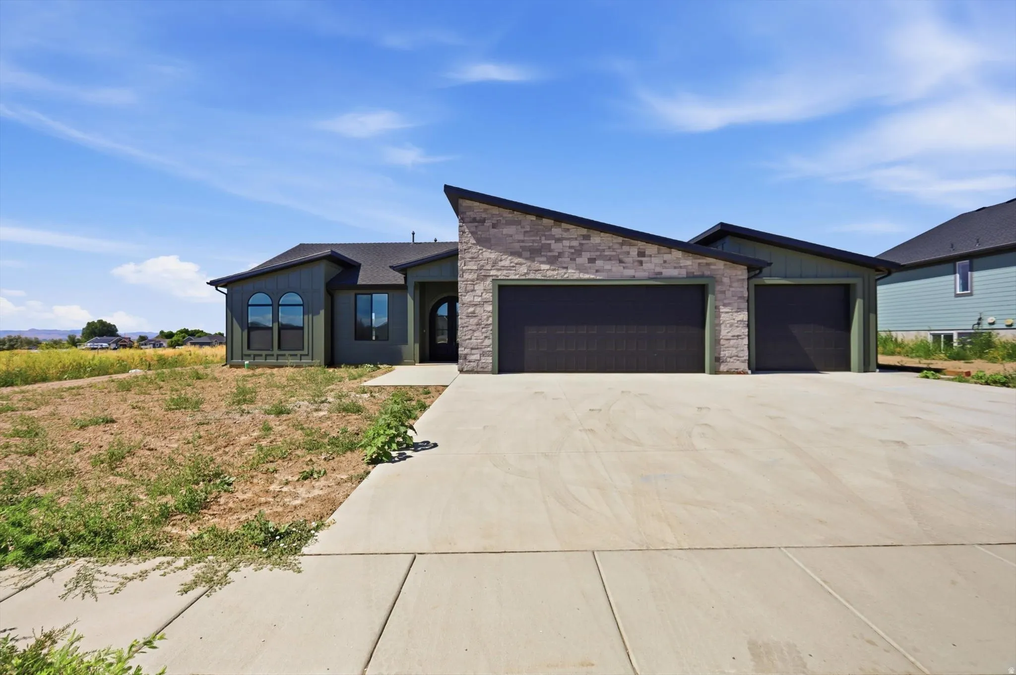 Modern architectural style featuring a stone and siding exterior, arched windows, and a concrete driveway