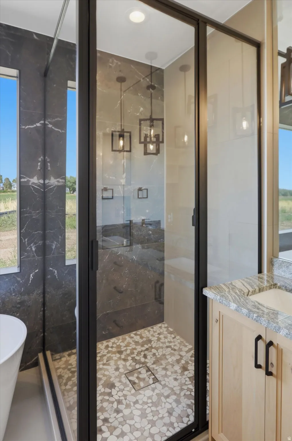 Frameless glass shower enclosure with a pebble-tile floor and dark-toned large format wall tiles