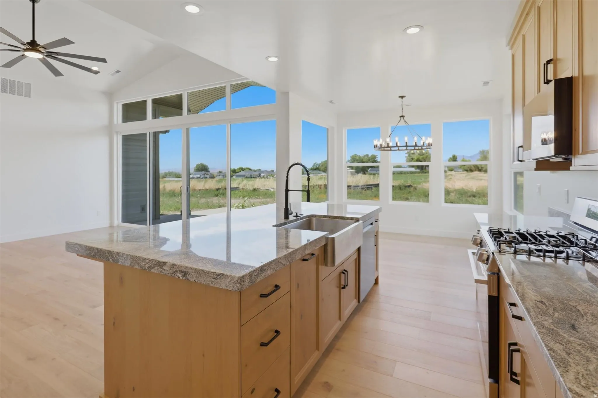 Kitchen featuring a center island with sink, gas range, wood-finish flooring, recessed lighting, and large windows