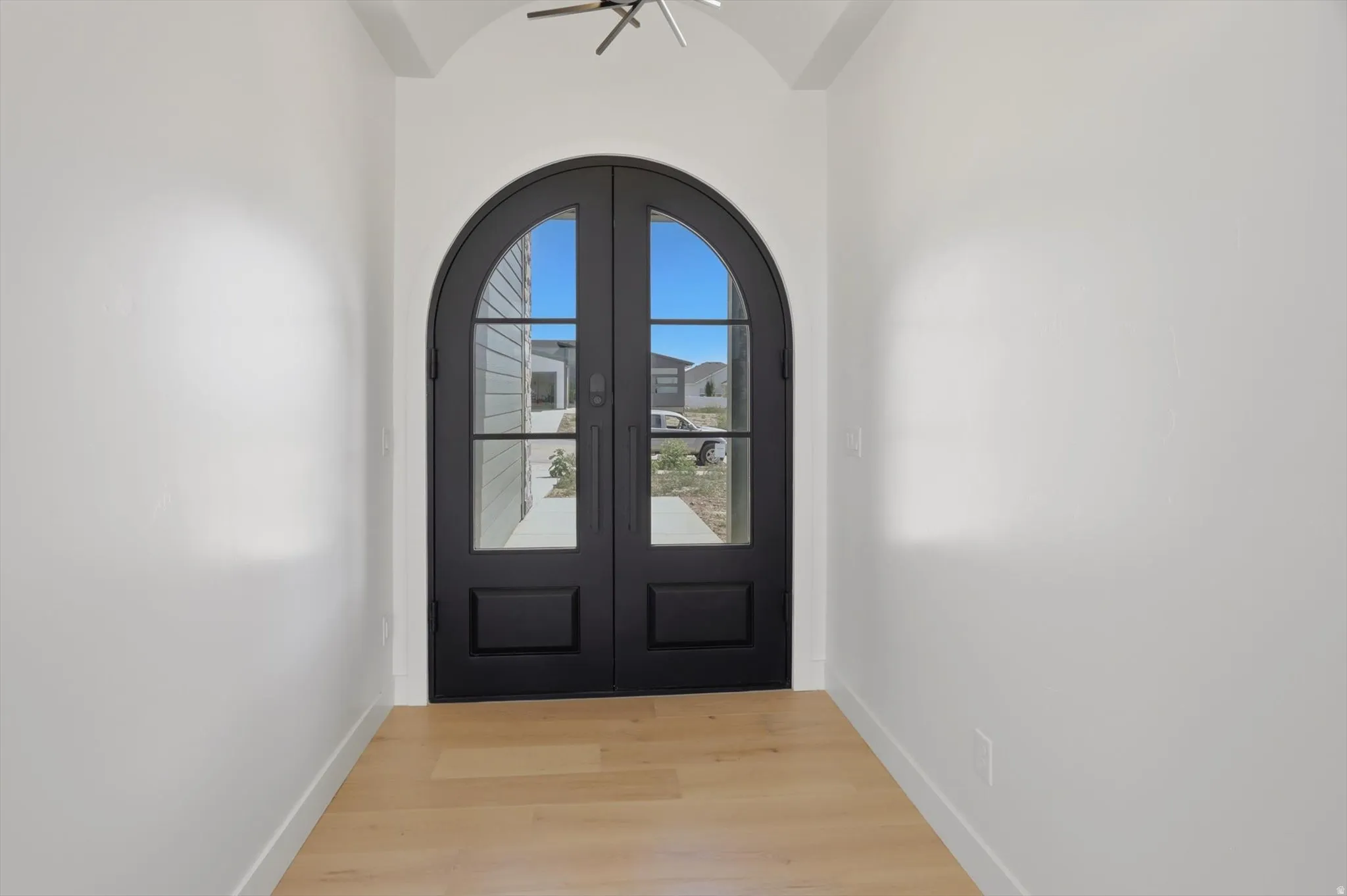 Arched double entry doors with integrated glass panels, light wood-finish flooring, and crisp white walls