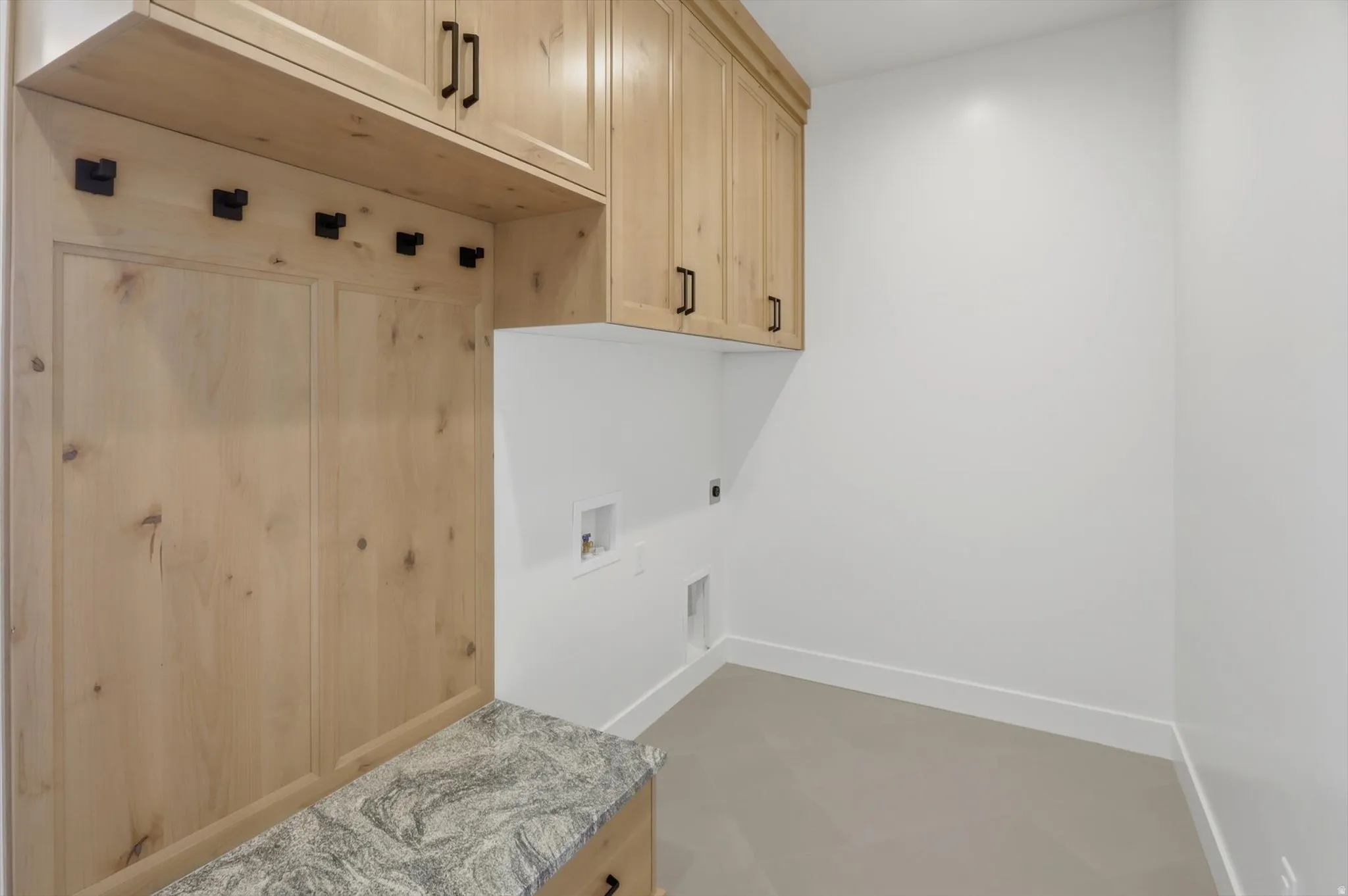 Hardwood cabinetry with black hardware, built-in coat hooks, and a stone-finish countertop
