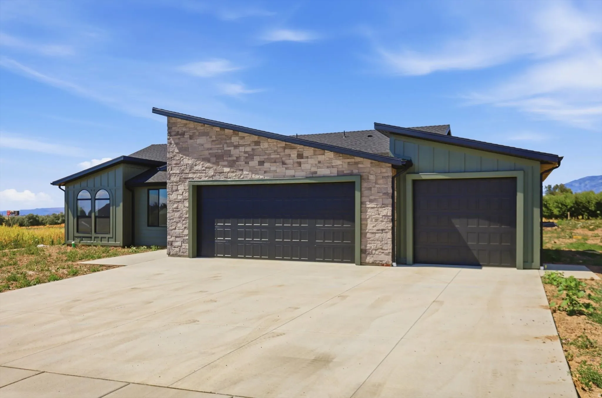 Contemporary exterior with stone accent, dual garage doors, and a concrete driveway