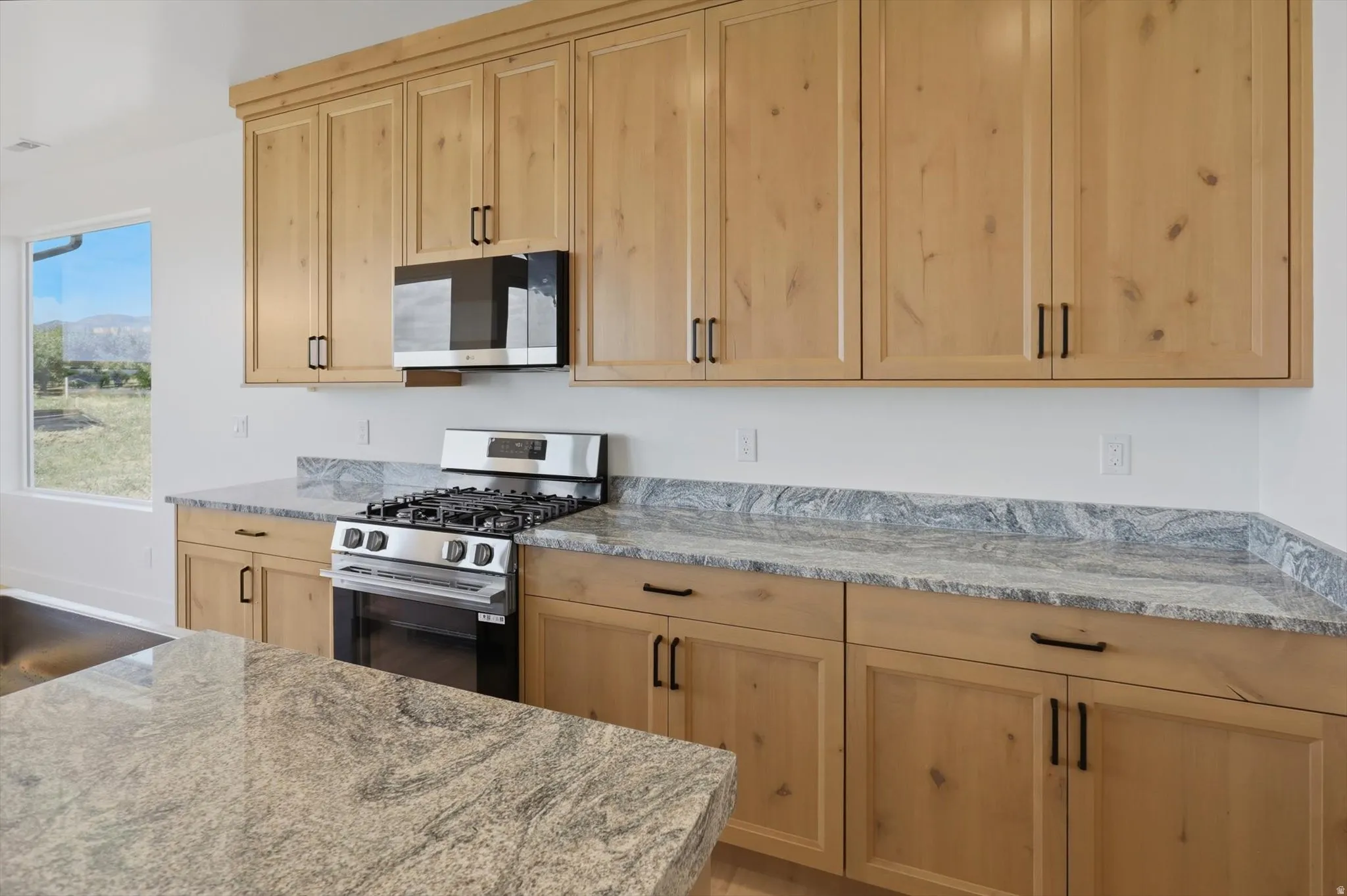 Light wood-finish cabinetry, stainless steel oven/range, built-in microwave, and stone countertops