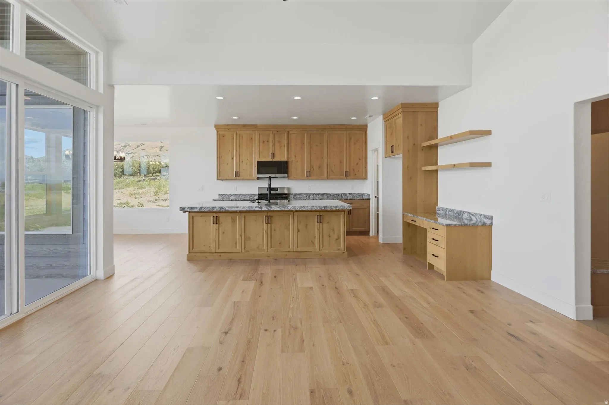 Open-concept living area with wood-finish flooring, a kitchen island, natural wood cabinetry, and a built-in desk area with floating shelves