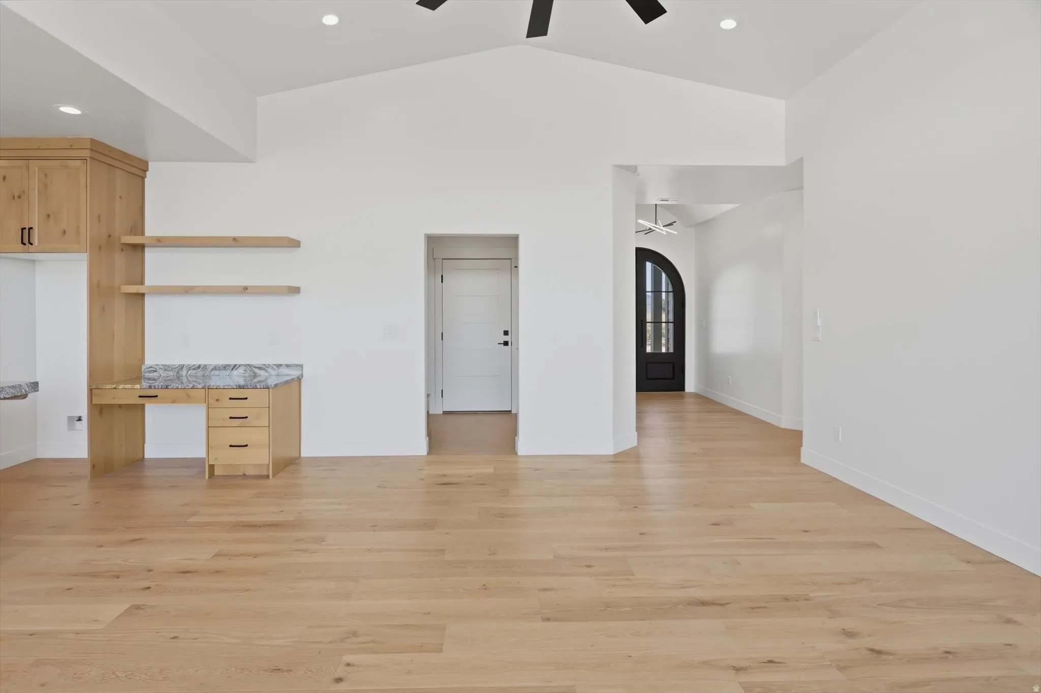 Light wood-finish flooring, vaulted ceilings, and a built-in wood desk with floating shelves and stone countertops