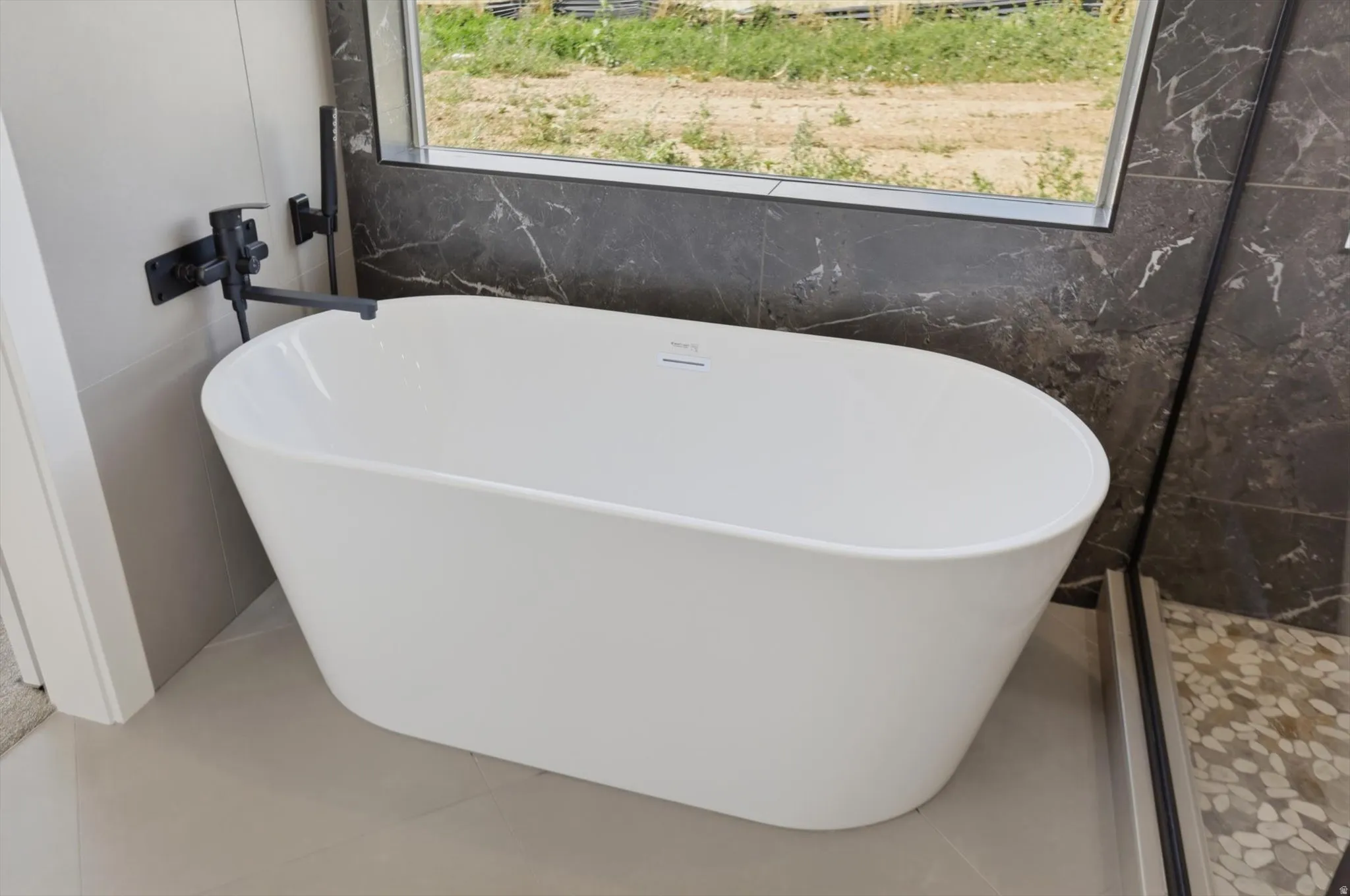 Freestanding soaking tub with matte black wall-mounted faucet, complemented by large format wall tile and a mosaic tile shower floor