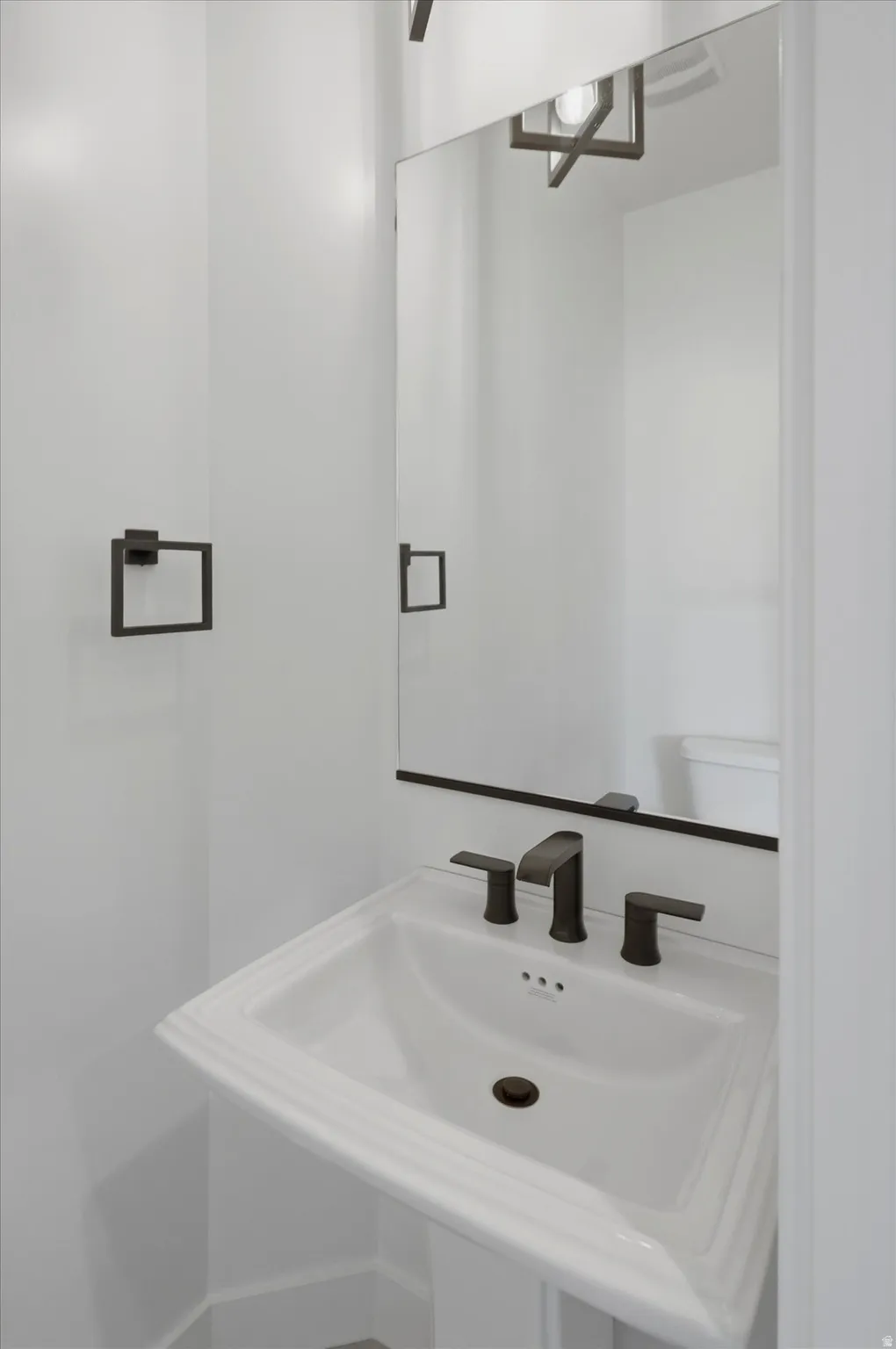 Pedestal sink with dark bronze faucet, framed mirror, and coordinating dark bronze towel ring