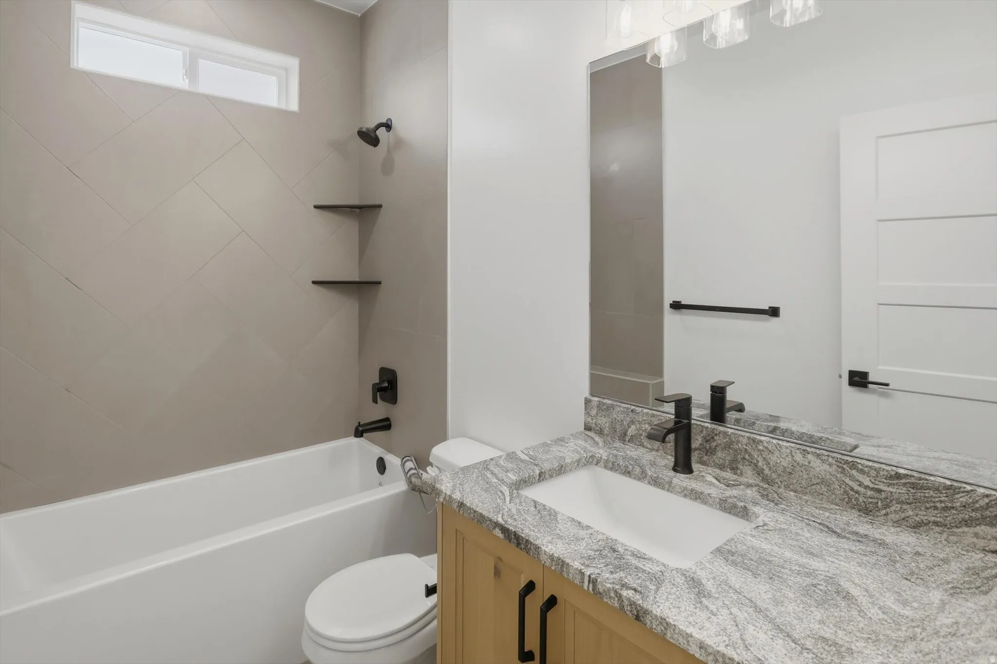 Bathroom featuring a tub/shower combination with tiled surround, wood-finish vanity with countertop, rectangular undermount sink, and black fixtures