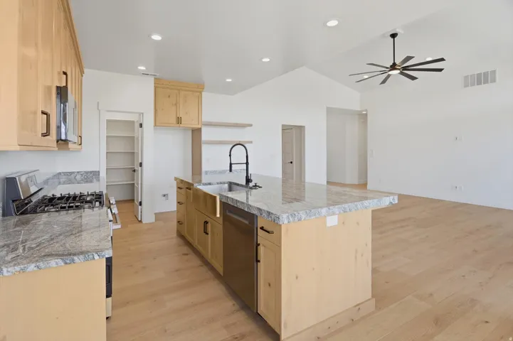 Kitchen featuring light wood cabinetry, stone countertops, a large center island with an undermount sink, and light wood-finish flooring