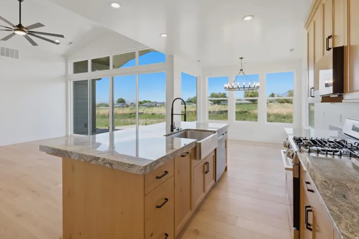 Kitchen featuring a center island with sink, gas range, wood-finish flooring, recessed lighting, and large windows