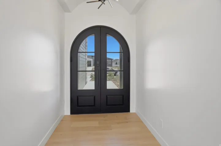 Arched double entry doors with integrated glass panels, light wood-finish flooring, and crisp white walls