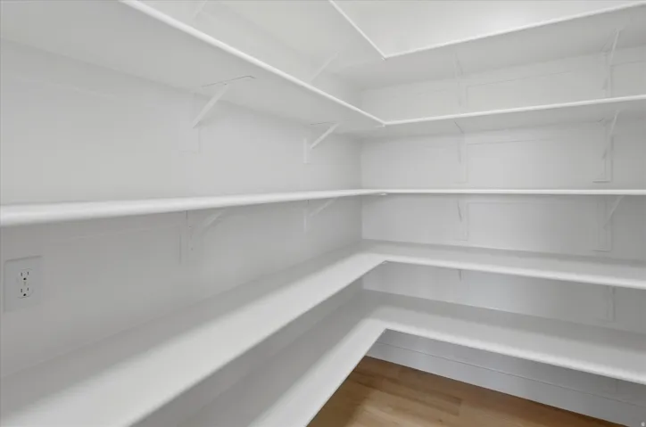 Walk-in pantry featuring extensive white shelving and light wood-finish flooring