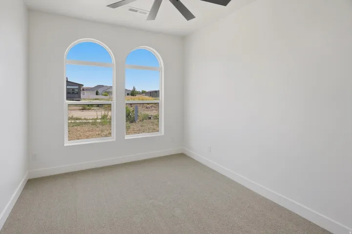 Arched windows, neutral carpet flooring, white painted walls, and a ceiling fan with integrated lighting