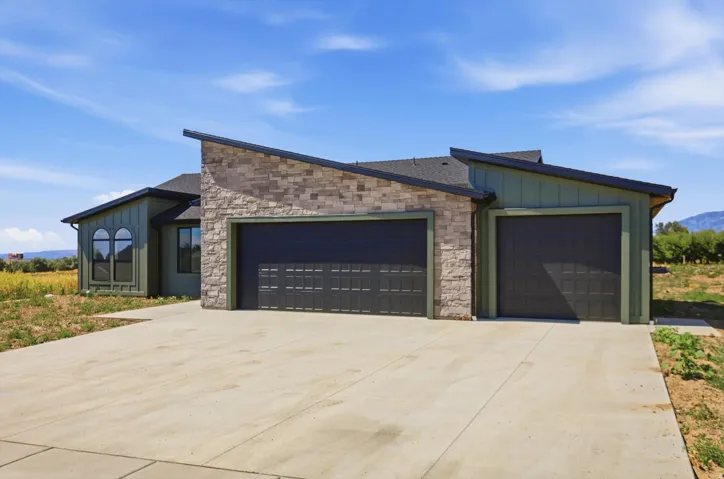Contemporary exterior with stone accent, dual garage doors, and a concrete driveway