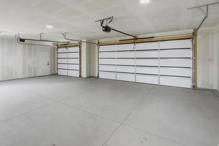 Spacious garage with concrete flooring, two overhead garage doors, and a dedicated entry door