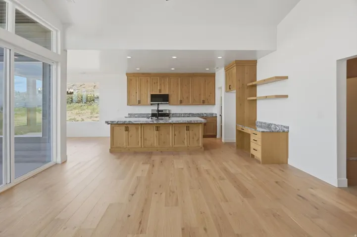 Open-concept living area with wood-finish flooring, a kitchen island, natural wood cabinetry, and a built-in desk area with floating shelves