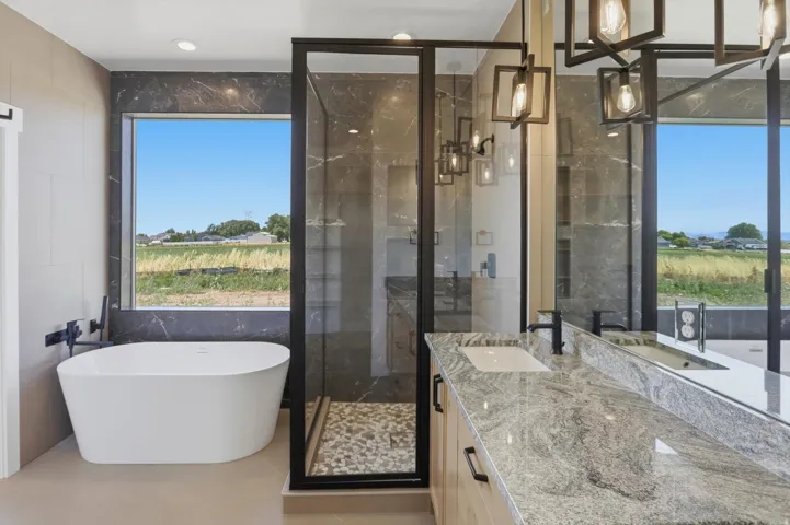 Freestanding soaking tub, walk-in shower with pebble floor, dual vanity with undermount sinks and stone countertop, and contemporary lighting fixtures