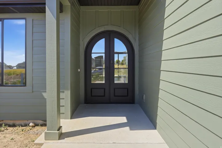 Arched double entry doors, durable concrete porch, window with dark trim, vertical and horizontal siding, and substantial support column