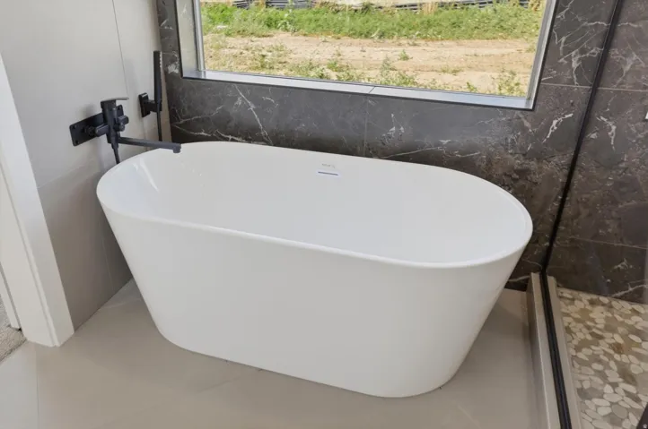 Freestanding soaking tub with matte black wall-mounted faucet, complemented by large format wall tile and a mosaic tile shower floor