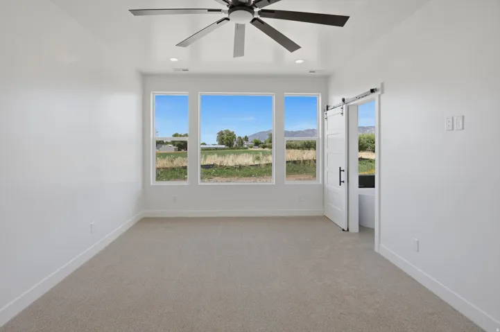 Recessed lighting, ceiling fan with dark finish, three large windows, carpeted flooring, and a barn door with dark hardware