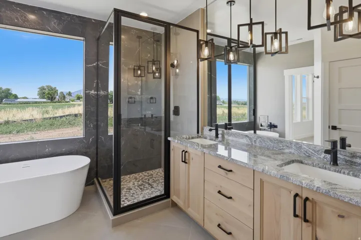 Freestanding soaking tub, black-framed glass shower enclosure with pebble floor, dual vanity with undermount sinks, and natural wood-finish cabinetry with black hardware