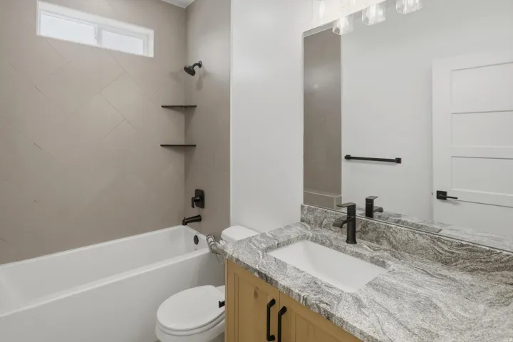 Bathroom featuring a tub/shower combination with tiled surround, wood-finish vanity with countertop, rectangular undermount sink, and black fixtures