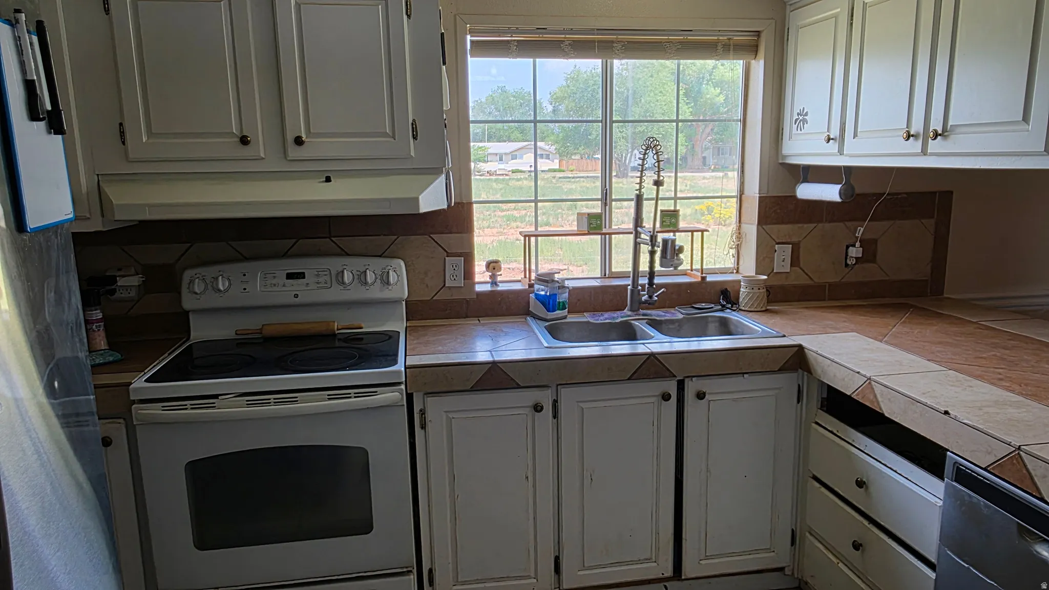 White cabinetry and appliances, tile countertops, and a double basin sink