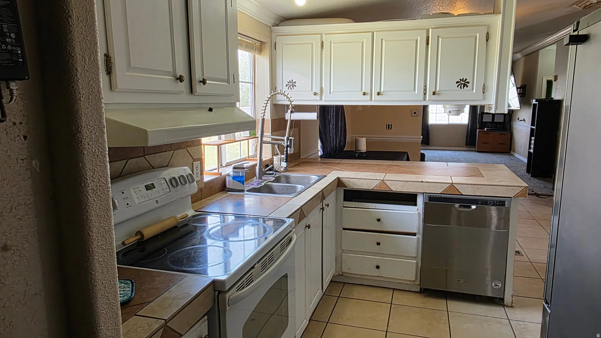 Kitchen featuring white cabinetry, tile countertops, stainless steel dishwasher, and a tile backsplash