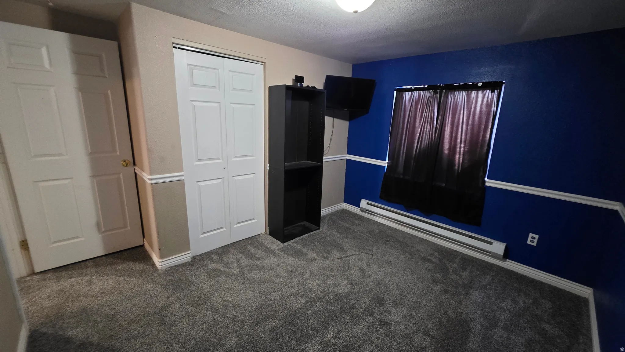 Grey carpet flooring, bi-fold closet doors, white paneled door, baseboard heating unit, and crown molding