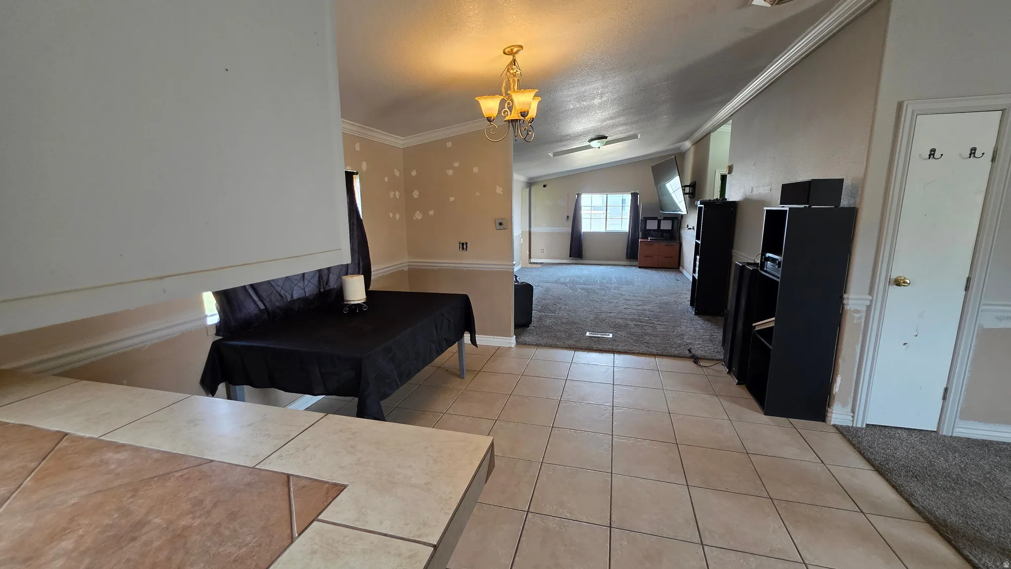 Tile flooring extending into a separate carpeted area, featuring an overhead chandelier