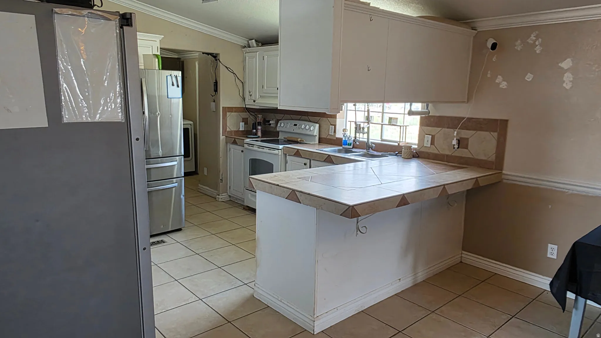 White cabinetry, tile flooring, stainless steel appliances, and a tiled breakfast bar