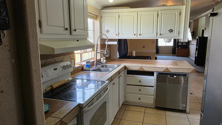 Kitchen featuring white cabinetry, tile countertops, stainless steel dishwasher, and a tile backsplash