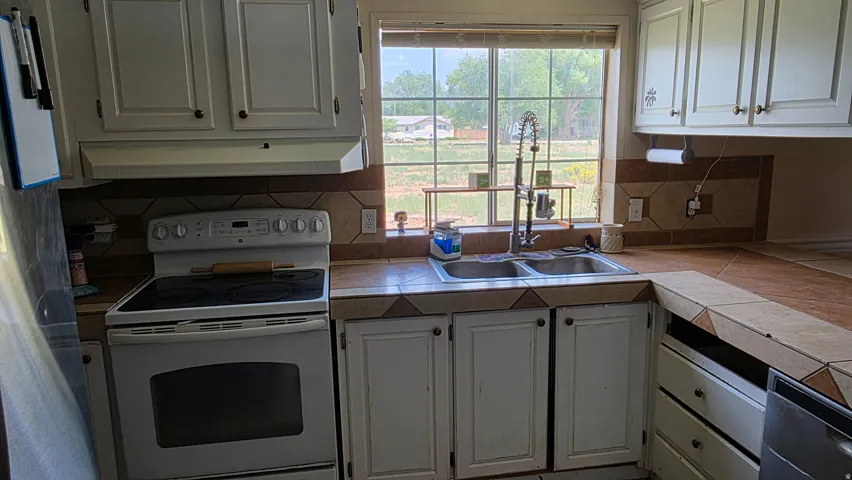 White cabinetry and appliances, tile countertops, and a double basin sink