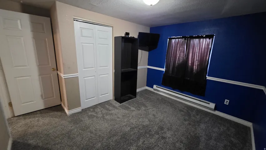 Grey carpet flooring, bi-fold closet doors, white paneled door, baseboard heating unit, and crown molding