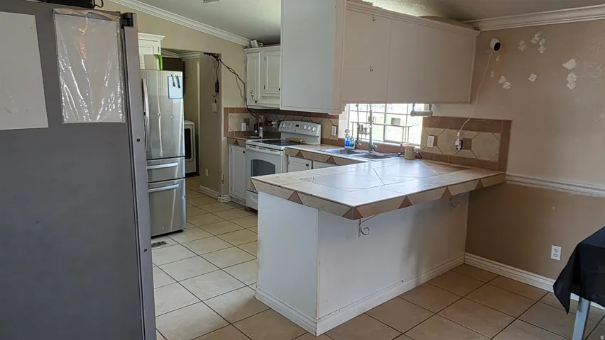 White cabinetry, tile flooring, stainless steel appliances, and a tiled breakfast bar