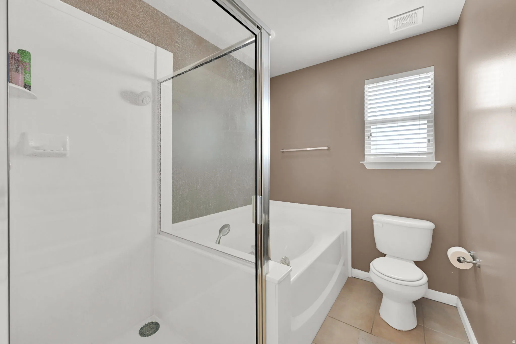 Walk-in shower with clear glass enclosure and built-in shelving, white bathtub, and toilet with tiled flooring