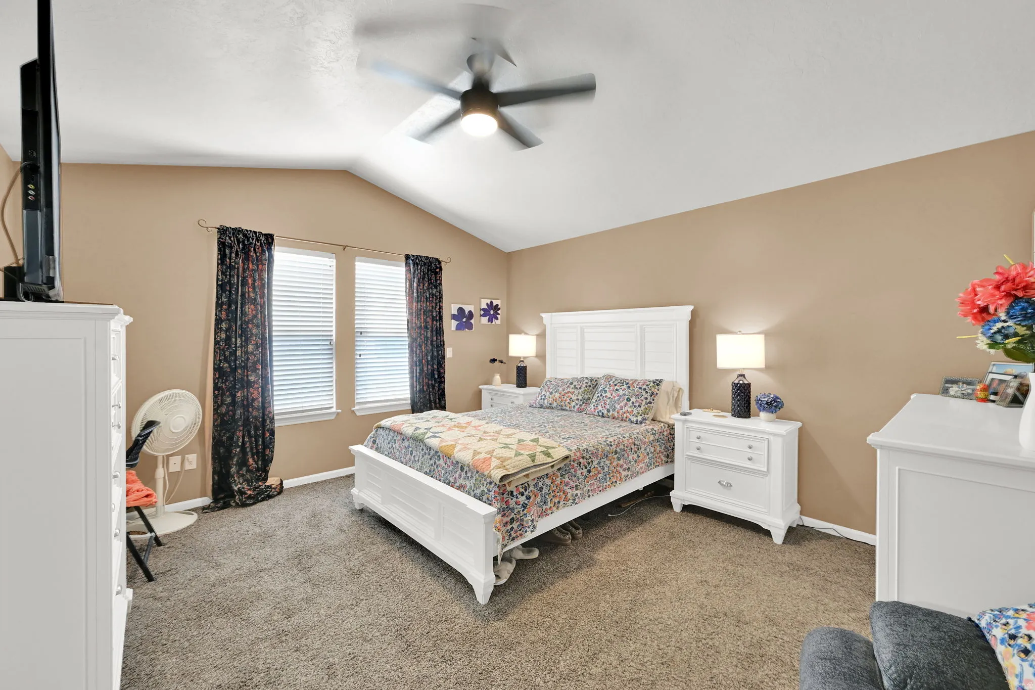 Vaulted ceiling with a ceiling fan, carpet flooring, and two windows with blinds