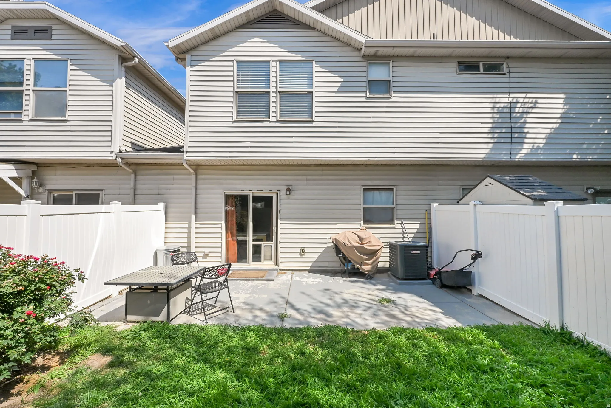 Rear exterior featuring horizontal siding, multiple windows, a sliding glass door, a concrete patio, and a white privacy fence