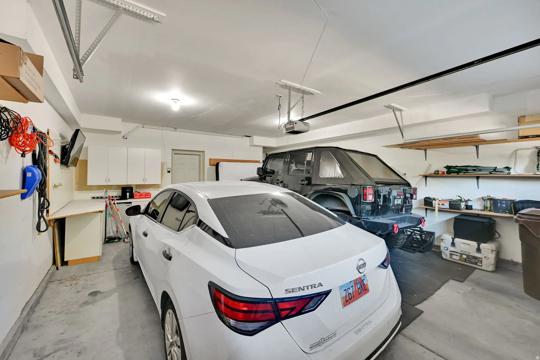 Two-car garage featuring overhead door openers, built-in shelving, white cabinetry, and a workbench