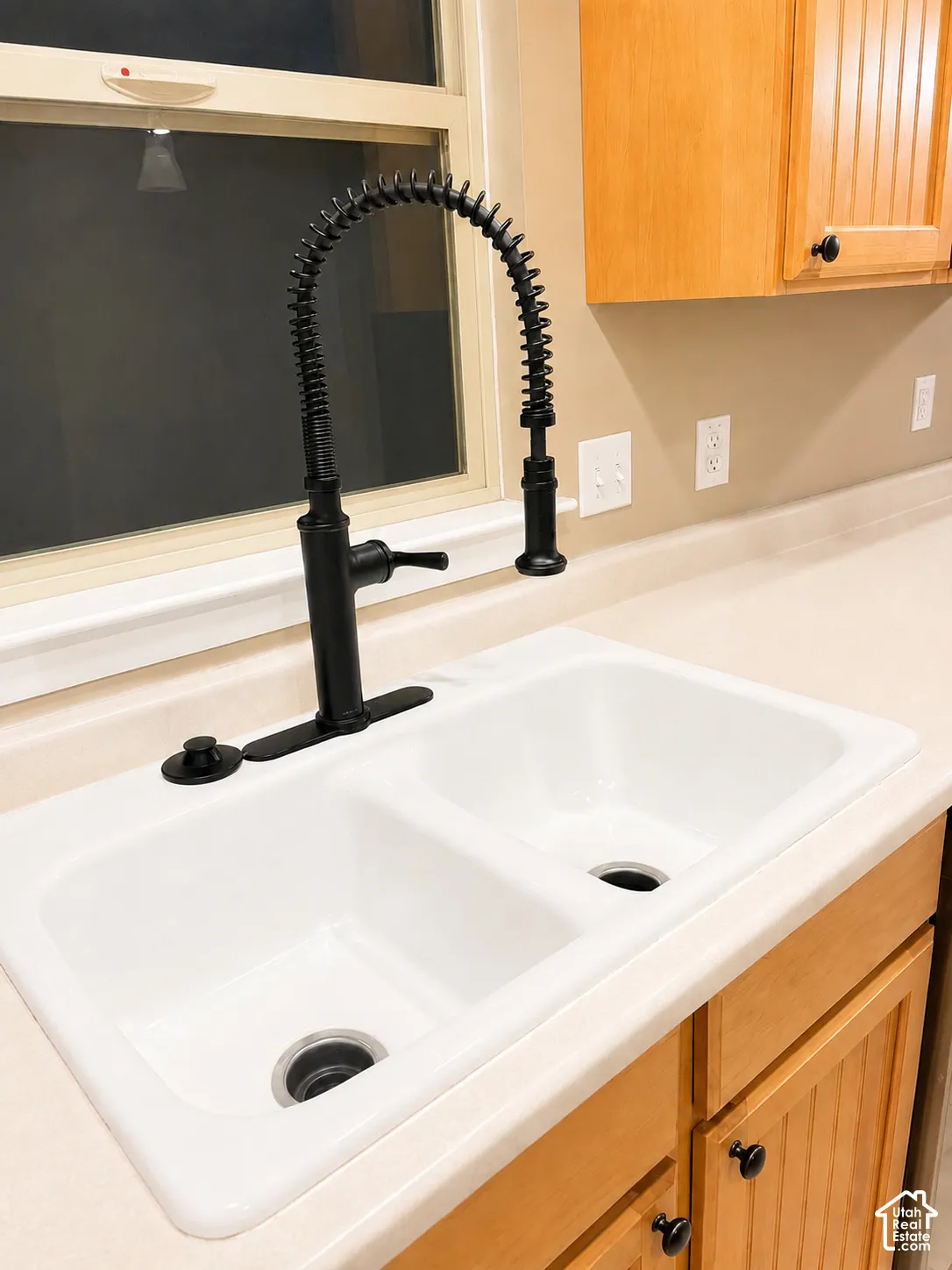 Dual-basin white sink with a matte black pull-down faucet, set into a light-toned countertop, complemented by light wood-finish cabinetry