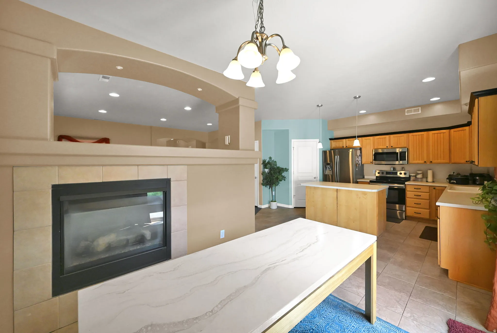 Gas fireplace with tile surround, wood-finish cabinetry, stainless steel kitchen appliances, kitchen island with countertop, and recessed lighting