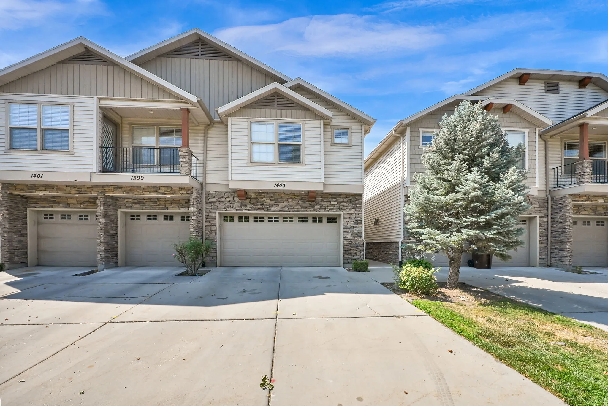 Multi-story townhome exterior featuring stone and siding finishes, individual garages with window accents, and a second-level balcony with metal railing